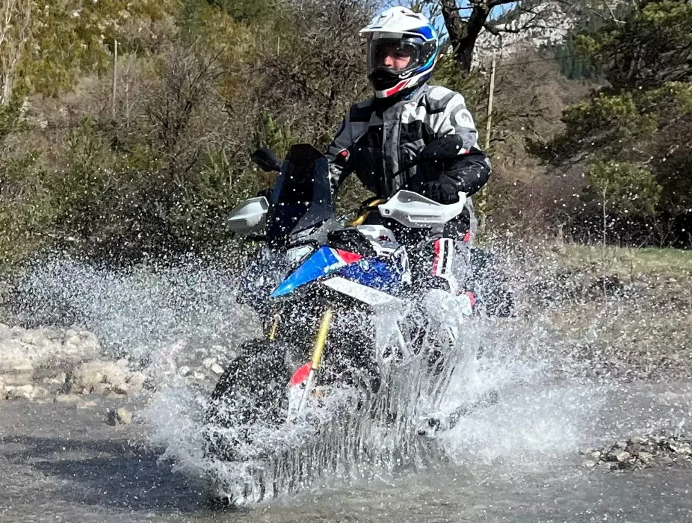 Une BMW F 450 GS Rally traversant un ruisseau, des gerbes d'eau et des arbres