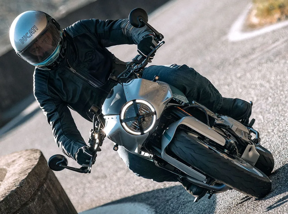 Un motard avec un blouson noir et un casque gris pilotant une moto Ducati Formula 73
