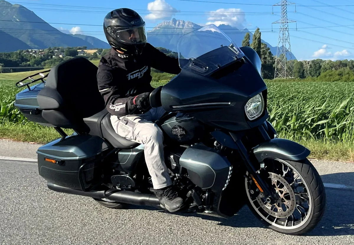Une moto Harley-Davidson Street Glide Limited sur la route, un champ, un pylône électrique, un ciel bleu et des montagnes
