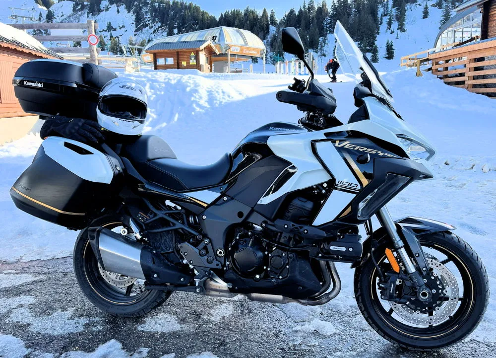 Une moto Kawasaki Versys 1100 SE blanche, de la neige et une station de ski