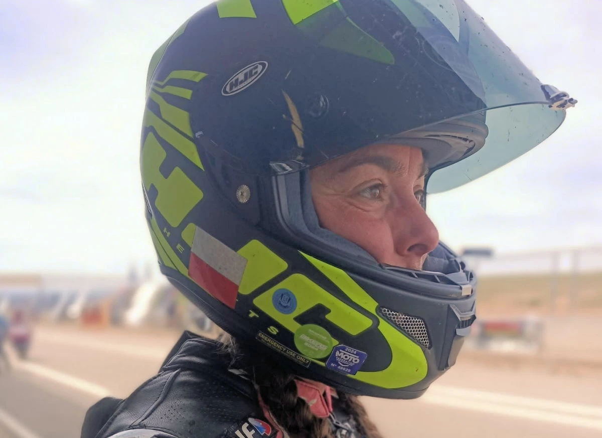 Une femme regardant avec sérieux, un casque moto avec la visière relevée et des grandes lettres jaunes