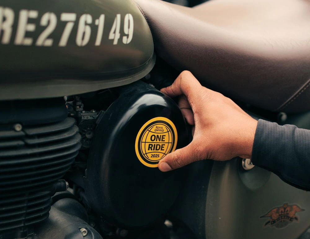 Une main posant un badge One Ride sur une Royal-Enfield