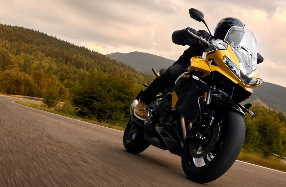 Une moto Triumph Tiger Sport 800 sur une route avec un paysage montagneux et forestier