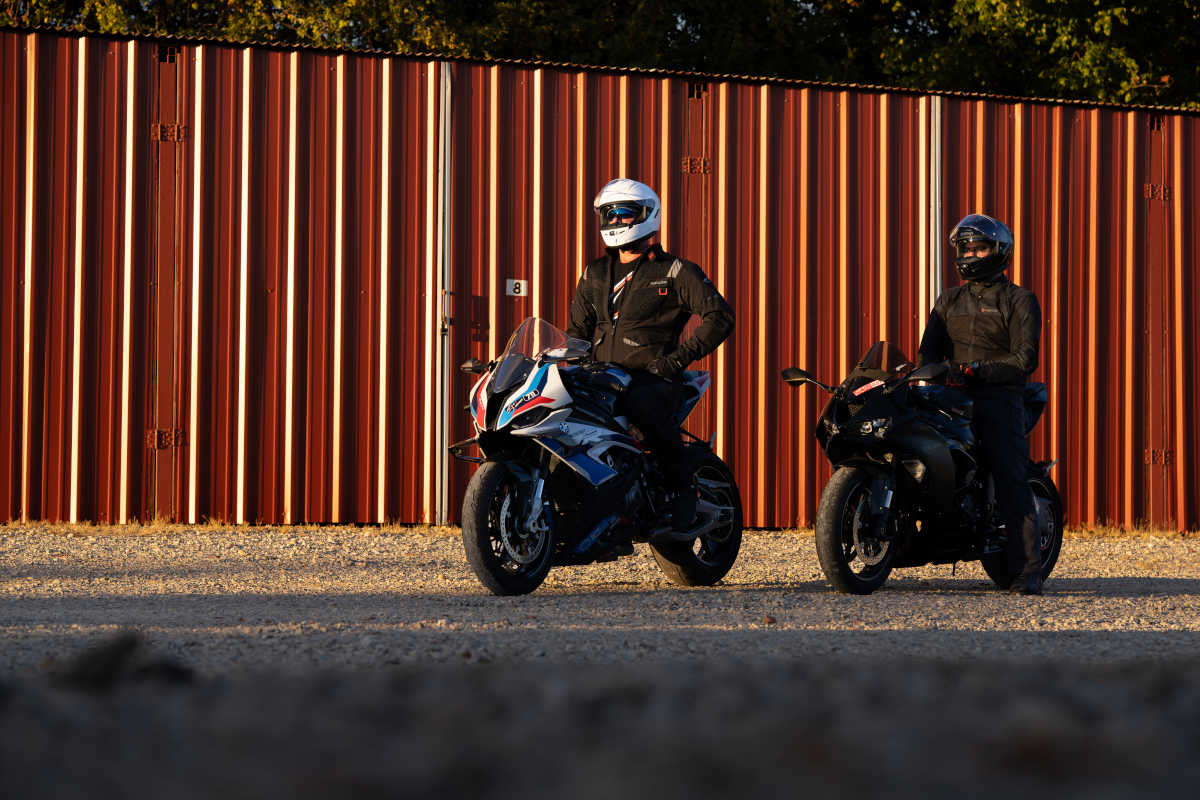 Two motorcyclists on motorcycles in front of a red warehouse