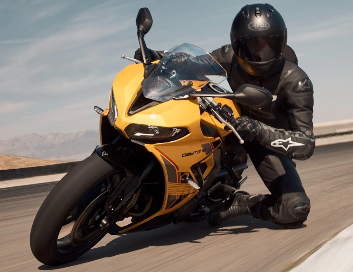 une moto Triumph 660 Daytona jaune et un motard habillé en noir dans une posture de virage sur l'angle