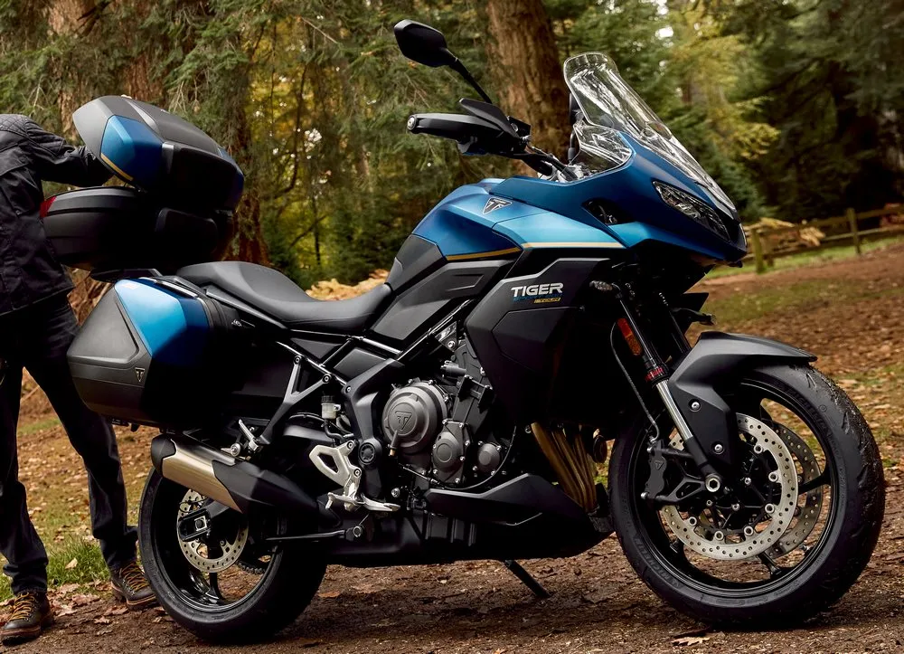 Une moto Triumph Tiger Sport 800 Tour de couleur bleu devant une forêt.